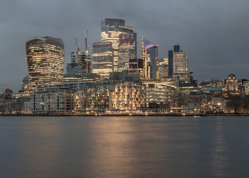London, UK - Feb 15, 2024 - The illuminated of skyscraper in the business district of London with reflections in the River Thames just after sunset. View of architectural modern buildings of the city, Space for text, Selective Focus.