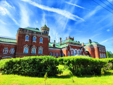 A striking red brick building featuring ornate towers and architectural details stands under a vivid blue sky streaked with delicate cirrus clouds