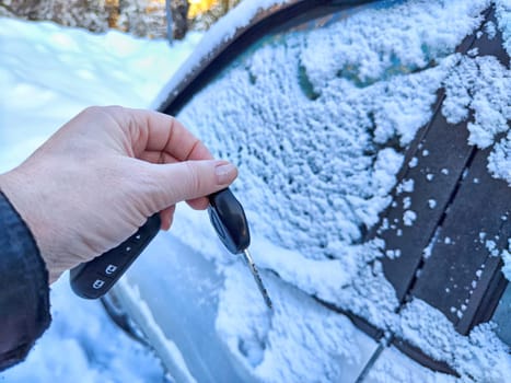 Woman Person Attempting to Unlock Car Covered in Snow by key on a Cold Winter Day. Finger holding key near the frozen lock of a snow-covered car, illustrating frozen car challenge