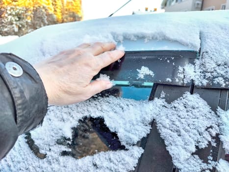 Hand of Woman persons brushing snow of car window, which frozen over during a bitterly cold morning. Problem with travel and trip in winter