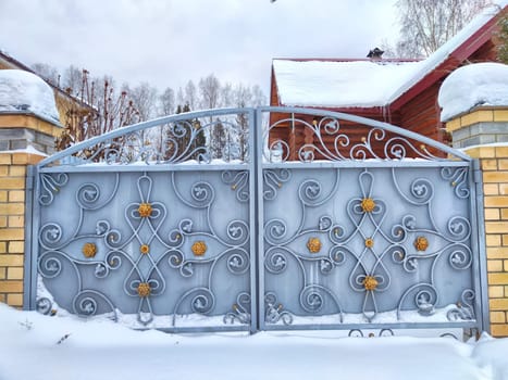 closed iron gate on a gray brick wall of a garage outside in white snow