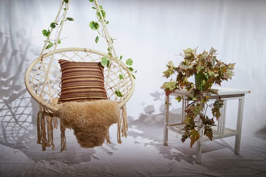 Modern cozy beautiful room with a braided rope macrame chair, green plants, small table and curtains. Interior and background. Location for photo shooting