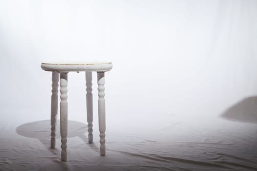 Solitary Wooden Stool in a White Minimalist Setting. Lone, white-painted wooden stool stands centered on textured surface, surrounded by soft white backdrop