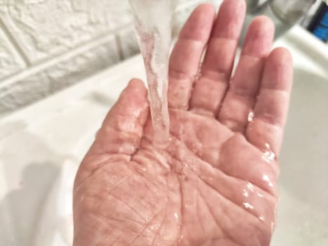 Water Flowing Onto an Open Hand in a Sink. detailed view of a stream of clear water pouring down onto the palm of hand. Concept of hygiene or the sensual pleasure