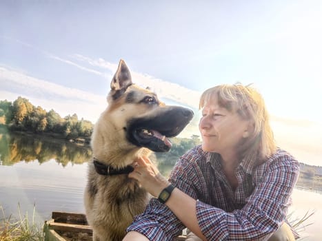 Adult girl with shepherd dog taking selfie in forest. Middle aged woman and big shepherd dog on nature. Friendship, love, fun, hugs