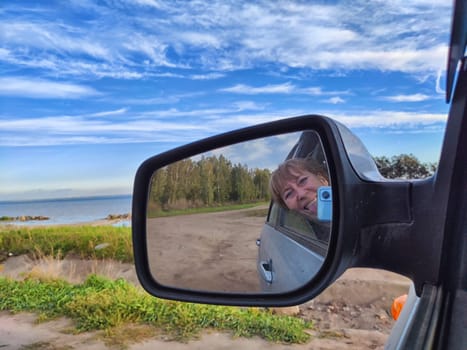 Self portrait at side view mirror of a car in travel, trip on nature