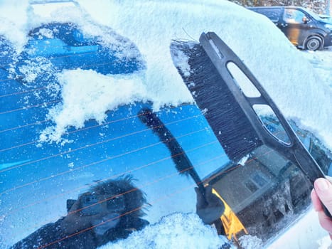 Winter Morning Car Snow Clearing. Woman person brushing snow off car on frosty winter morning and taking selfie in the reflection. Difficulties in travel and trip in cold months