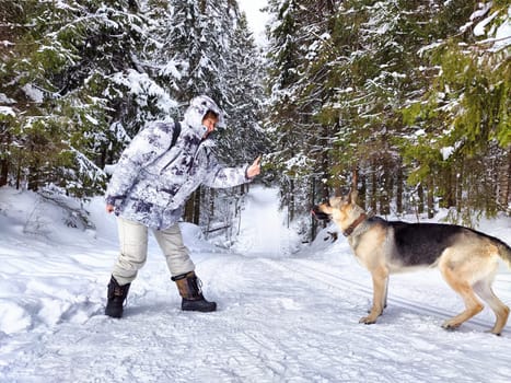 Adult girl or mature lady with shepherd dog in winter nature landscape in forest. Middle aged woman training big shepherd dog in cold day. Friendship, love, communication, fun, hugs