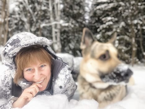 Portrait of Middle aged woman, adult girl, mature lady taking selfie with shepherd dog in snow winter nature landscape in forest in cold day. Fun, hugs. Partial focus