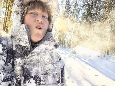 Cheerful middle aged woman in a winter warm sports jacket taking selfie on cold snow forest in nature outdoors. Steam from mouth in very cold weather