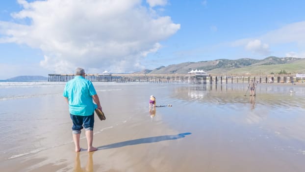Father and daughter enjoy a leisurely winter walk along the picturesque Pismo Beach, sharing quality time together amid the serene backdrop of gently crashing waves.