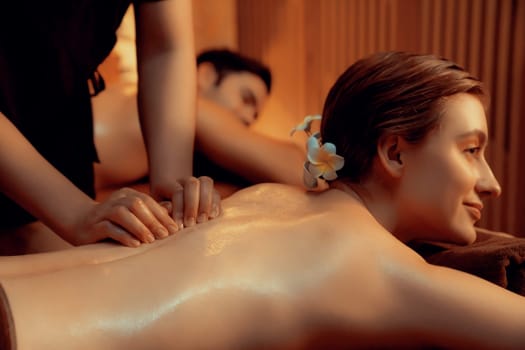 Caucasian couple customer enjoying relaxing anti-stress spa massage and pampering with beauty skin recreation leisure in warm candle lighting ambient salon spa at luxury resort or hotel. Quiescent