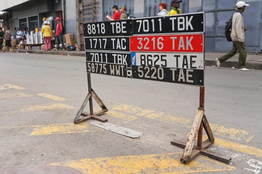 Antananarivo, Madagascar - April 24, 2019: Car license plates displayed near road (at auto garage shop), blurred people walking in background