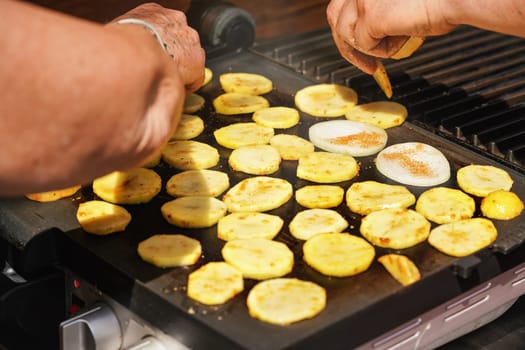 Senior women hands over grill with sliced potatoes