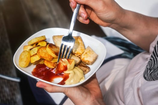 Woman hand holding fork and plate with grilled potatoes, and tofu (soy bean curd) with ketchup and mustard - vegetarian barbecue / grilling