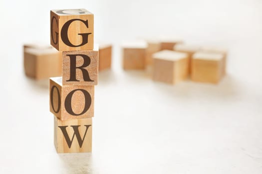 Four wooden cubes arranged in stack with text GROW on them, space for text / image at down right corner