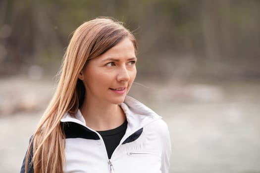 Portrait of young woman in white sports jacket on blurred outdoor background