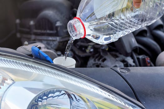 Pouring distilled water (ecological alternative to washing fluid) to washer tank in car, detail on liquid flowing from clear plastic bottle