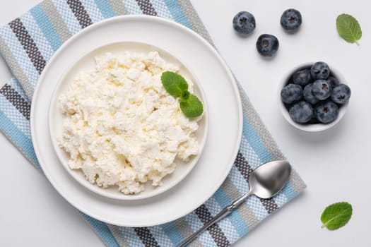 Cottage cheese with blueberry and mint on a white table. Cottage cheese in a bowl. Top view. Dairy products.