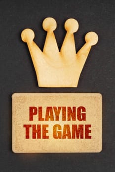 Business concept. On a black background there is a wooden crown of the leader and a sign with the inscription - Playing the Game
