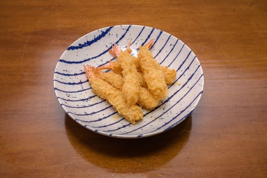 Shrimp tempura on a plate placed against a black background. Tempura is a Japanese food. It is Japanese fried shrimp