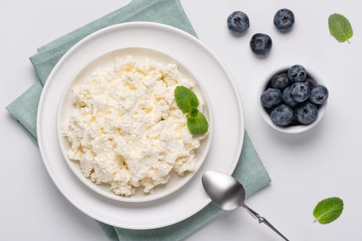 Cottage cheese with blueberry and mint on a white table. Cottage cheese in a bowl. Top view. Dairy products.