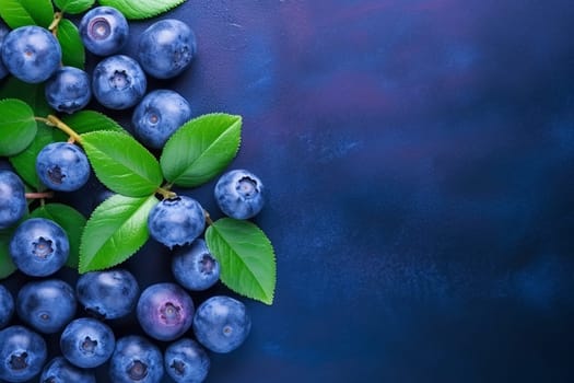 Fresh blueberries with green leaves on a blue background.