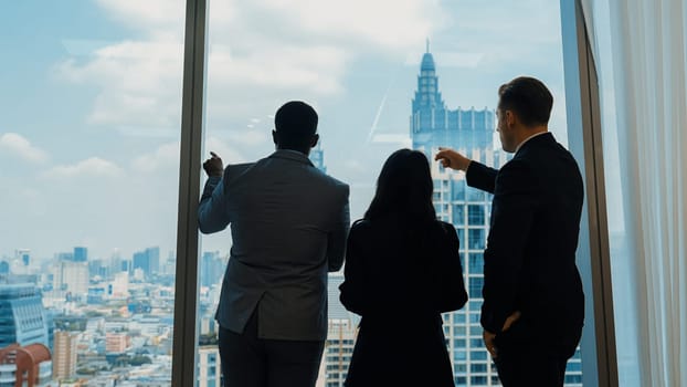 Back view diverse team of ambitious business people standing in ornamented office gazing out window to cityscape skyline. Determination and business ambition drive their career toward to bright future