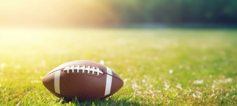 Close-up of an American football on green grass with sunlight in the background, suggesting a game or practice session.