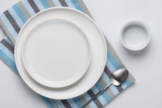 White empty plate with spoon and napkin on white background.