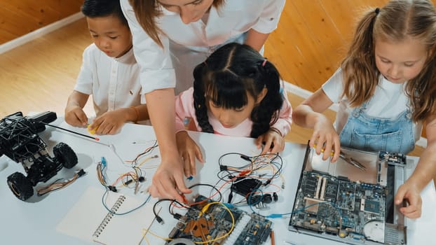 Top view of caucasian teacher teaching diverse students about electronic board. Multicultural children learn about digital electrical tool and fixing motherboard by using chips and wires. Erudition.