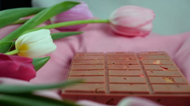 A bar of pink ruby chocolate with sublimated freeze-dried strawberries and almonds and spring tulip flowers . A dessert based on berries and nuts for International Women's Day, March 8, mother's day