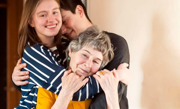 Young boy and a girl happily hug their grandmother, the family lovingly takes care of their elderly parents and congratulates them on the holiday, the grandson with his sister visit an elderly woman.