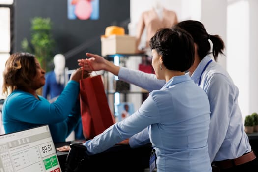 Fashion store employee giving bag to customer after paying for fashionable clothes in modern boutique. African american woman purchasing new fashion collection and stylish accessories