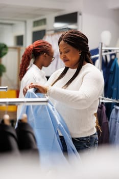 African american woman customer examining shirt on hanger in fashion boutique. Client shopping in mall clothing store and bringing modern formal wear apparel to fitting room