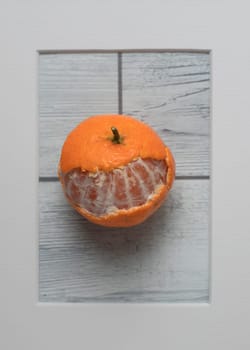 Partially peeled tangerine in frame on white wooden background