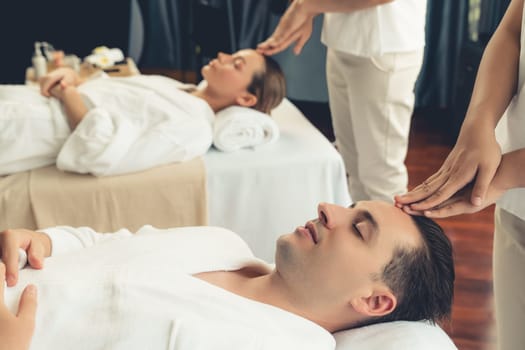 Caucasian couple enjoying relaxing anti-stress head massage and pampering facial beauty skin recreation leisure in dayspa modern light ambient at luxury resort or hotel spa salon. Quiescent