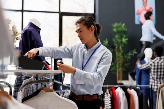 Asian man checking formal belt on store shelf, arranging stylish accessories in clothing store. Shopping mall worker loooking at with fashionable clothes. Fashion new collection concept