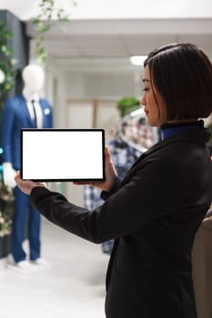 Clothing store asian woman consultant holding digital tablet white display mockup to showcase apparel information. Boutique assistant showing empty touchscreen for garment promotion