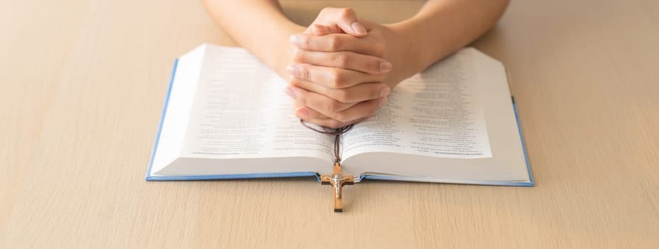 Cropped image of praying male hand holding cross on holy bible book at wooden table. Top view. Concept of hope, religion, faith, christianity and god blessing. Warm and brown background Burgeoning.