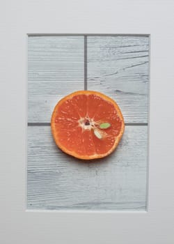 Mandarin slice in frame on white wooden background