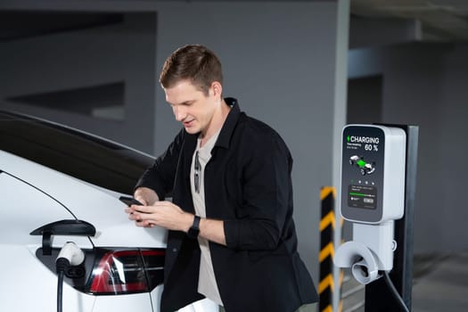 Young man travel with EV electric car to shopping center parking lot charging in downtown city showing urban sustainability lifestyle by green clean rechargeable energy of electric vehicle innards