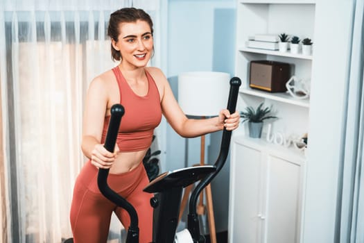 Athletic and sporty woman running on elliptical running machine during home body workout exercise session for fit physique and healthy sport lifestyle at home. Gaiety home exercise workout training.