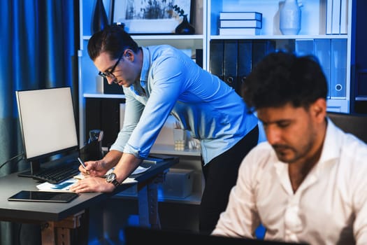 Colleagues concentrating on their job task at night home office behind desk while another man with thoughtful face solving to postpone the deadline of project at the blurred front side. Sellable.