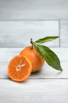 A whole tangerine with the leaf and a cut out slice on a white wooden background