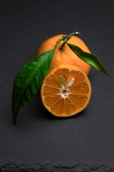 A whole mandarin with the leaf and a cut out slice on a black background