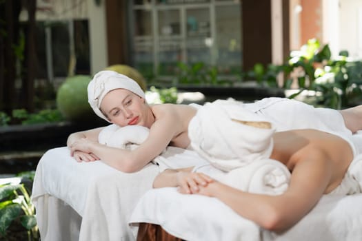 A portrait of a couple of a beautiful young caucasian woman with white towel rest on comfortable spa bed with relaxation while having body massage with professional masseur at spa salon.Tranquility.