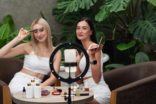 Two beautiful content creator making natural beauty and cosmetic tutorial on green plant garden video. Beauty blogger use camera light ring to show how to beauty care to social medial audience. Blithe