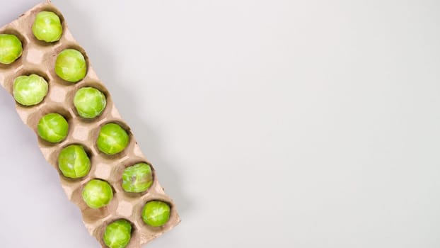 Raw organic Brussel sprouts in brown egg container on grey background, top view. Flat lay, overhead, from above. Copy space