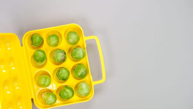 Raw organic Brussel sprouts in yellow container on grey background, top view. Flat lay, overhead, from above. Copy space